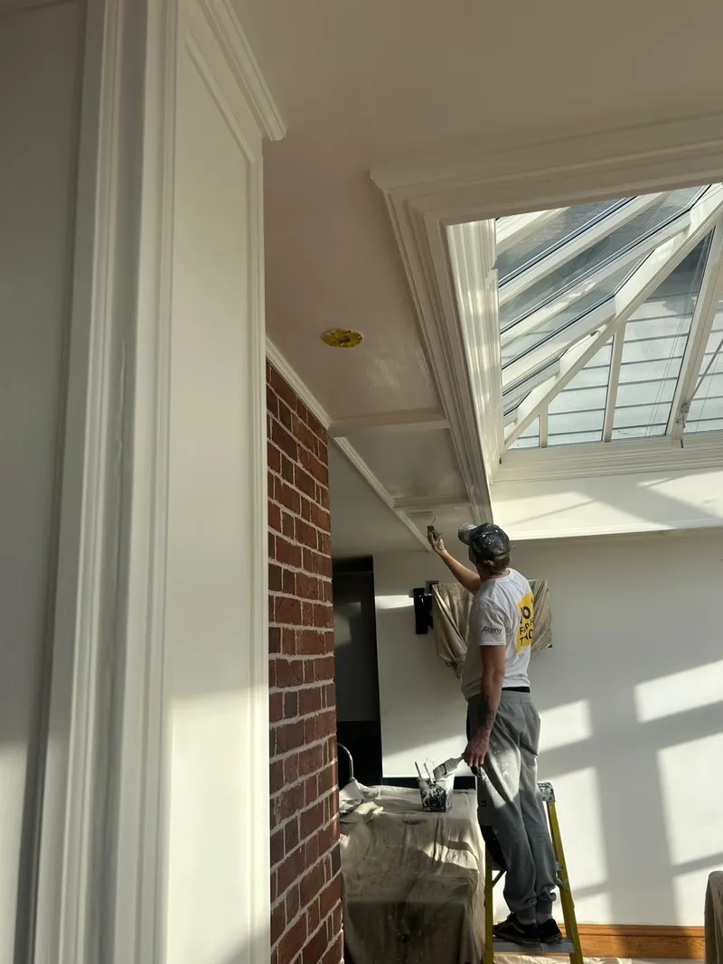 Painter on a step ladder brushing the coving beneath a glazed lantern roof